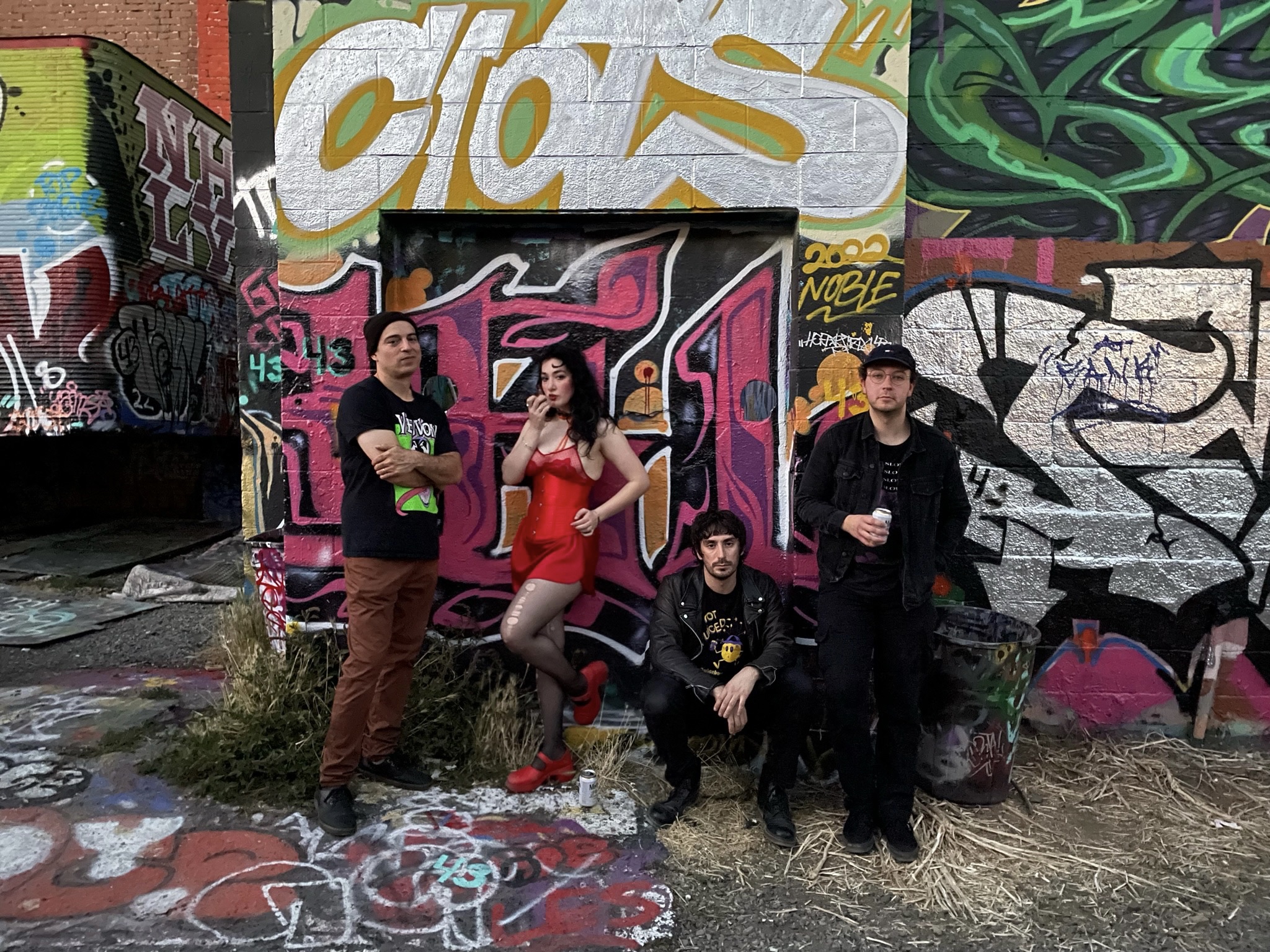 Fauxes musical quartet posed in front of a graffiti-covered wall.