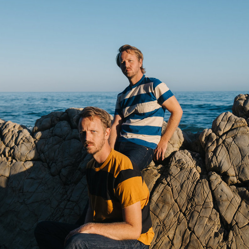Brothers Zach and Ben Yudin (aka Cayucas) sitting on the rocky shore of Southern California.