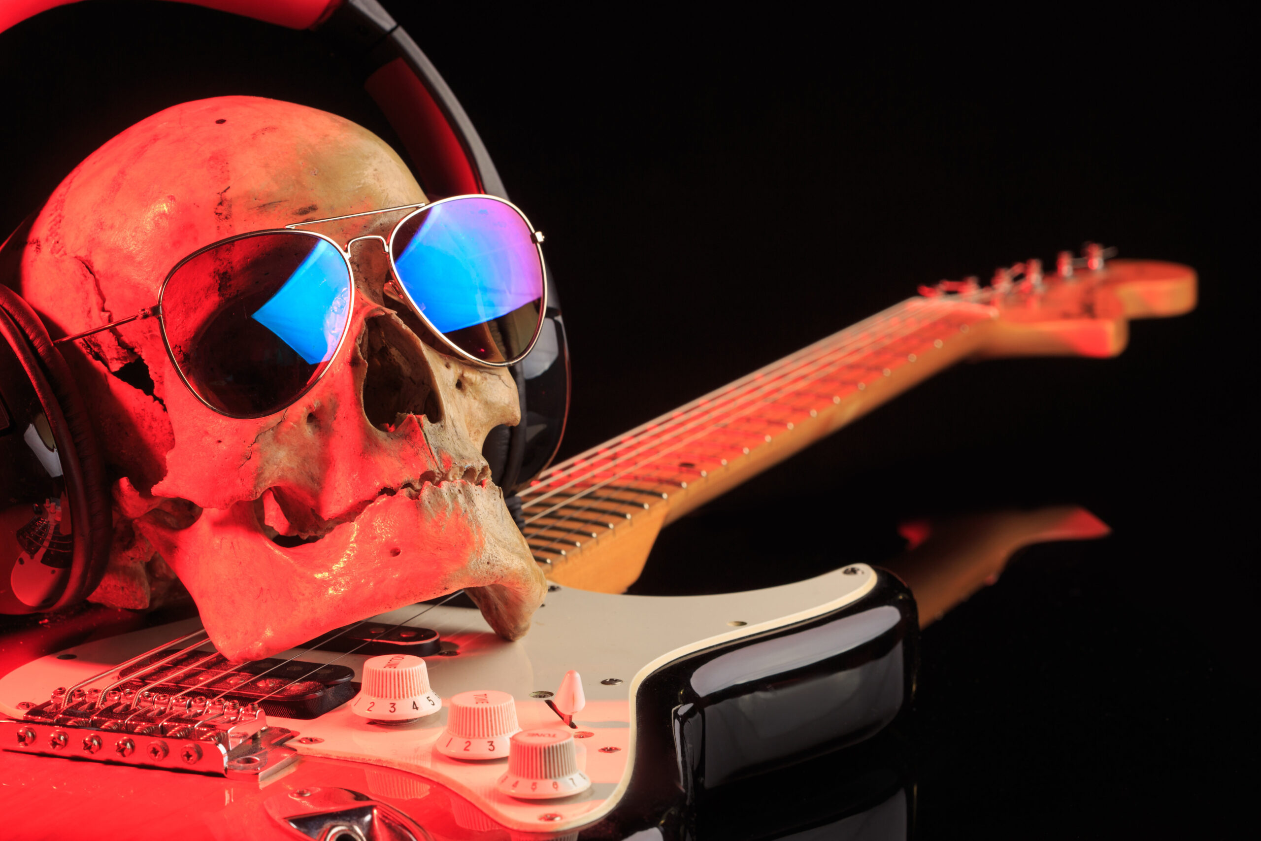 A skull wearing headphones and aviator sunglasses sits on a Telecaster style guitar.