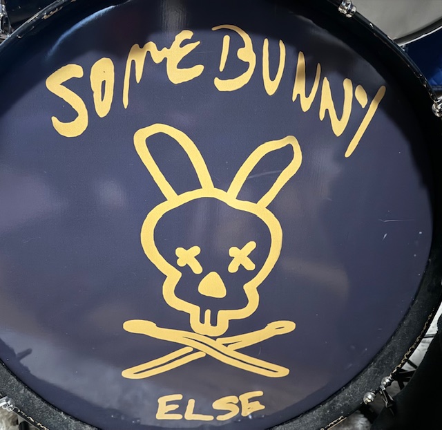 A bassdrum head painted with Somebunny Else's name and logo, which is a line drawing of a rabbit head with X'ed out eyes and crossed drumsticks below like a funny pirate flag.