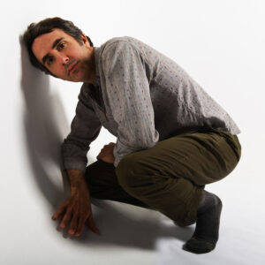 Chris Cohen squatting down in a white room.