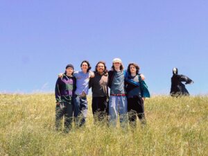 Five members of a band standing at the top of a hill with a shadowy figure in the background