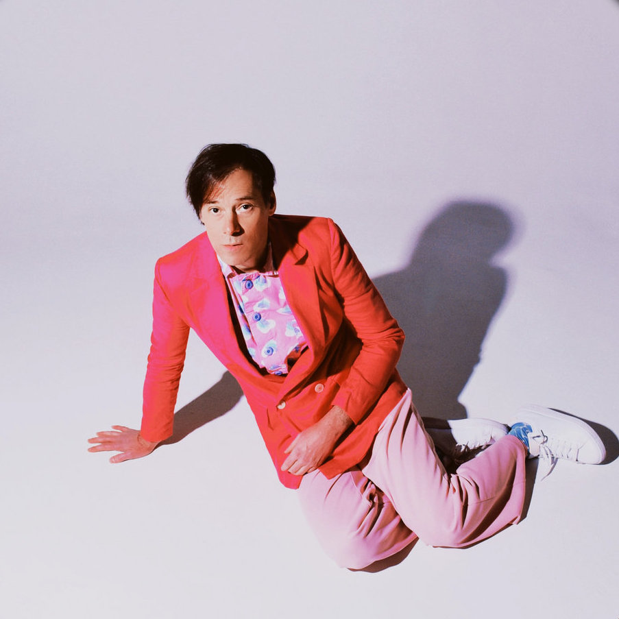 Kevin Barnes sitting on the floor in an empty white room.