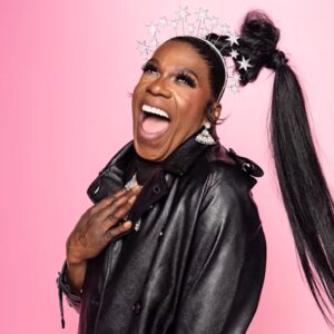 Big Freedia in a leather jacket with a pink background.
