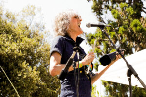 A woman performing on stage singing into a microphone holding a cowbell