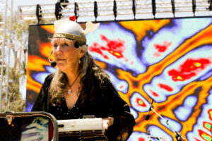 A woman wearing a viking helmet and microphone headset singing alongside a keyboard