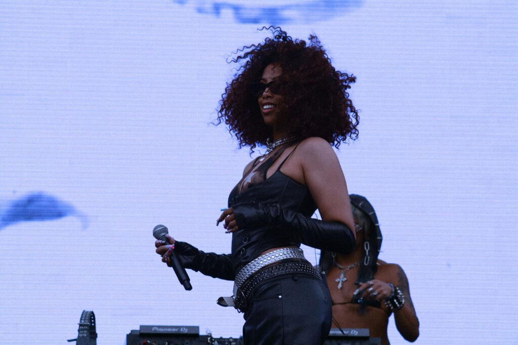 A woman on stage smiling holding a microphone with their DJ in the background