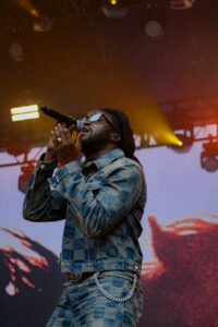 Man wearing denim jeans and jacket with sunglasses singing into a microphone on stage