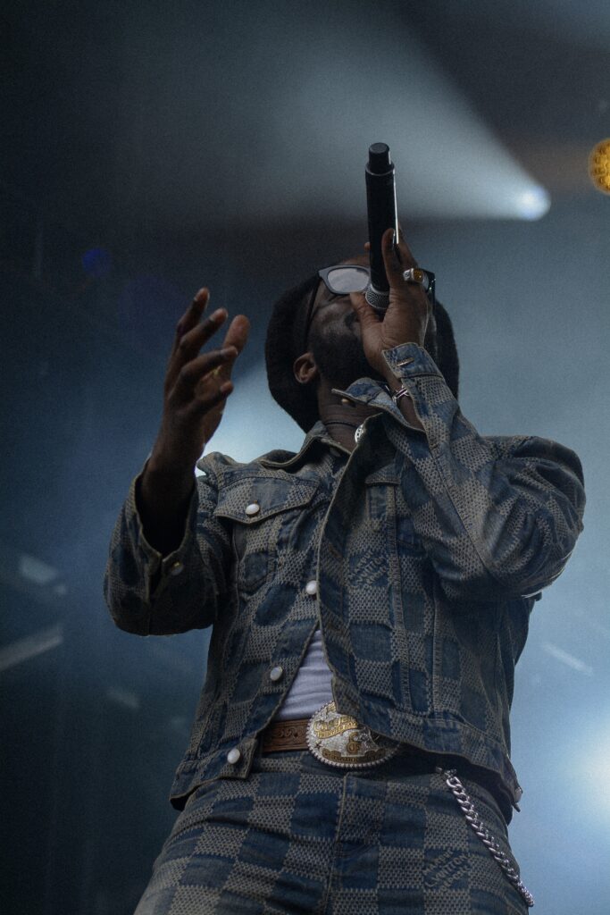 Man wearing denim jeans and jacket with sunglasses singing into a microphone on stage