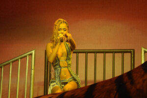 Woman in ripped denim singing into a microphone on stage pointing out to the crowd