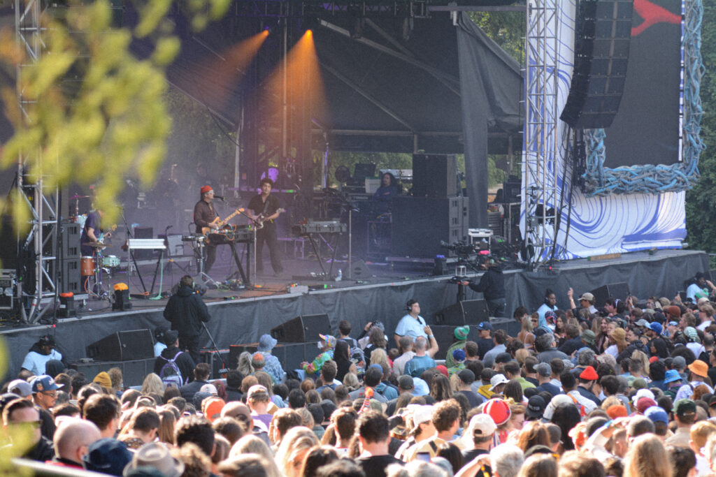 A rock band performing outdoors on stage in front of a large crowd