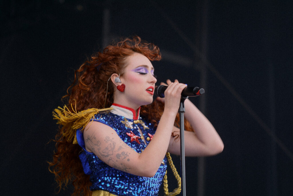 Performer singing into a microphone on stage wearing a sequin covered red, white, and blue outfit