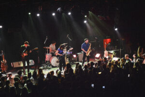 Rock band performing on stage with drums, bass, guitar, and singer