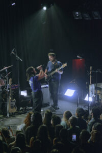 Woman singing into a microphone alongside a man playing bass guitar on stage