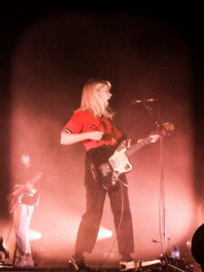 Vocalist/guitarist of the rock band Alvvays playing her instrument on stage in a red glow