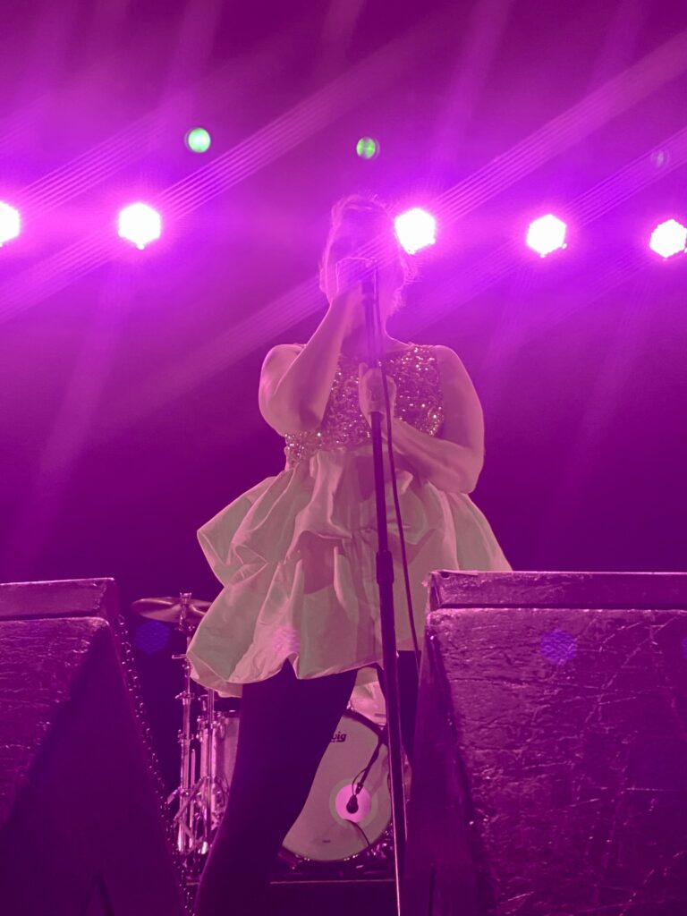 Singer performing on stage in a purple glow of lights