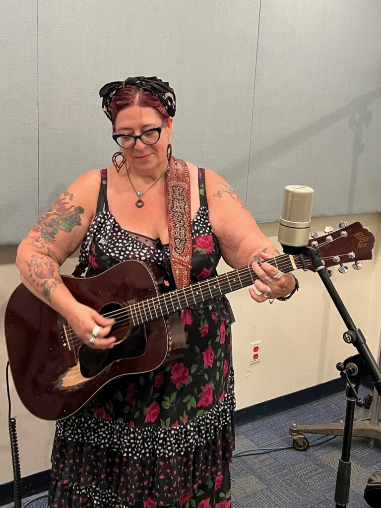 Woman playing an acoustic guitar in a studio in front of a microphone