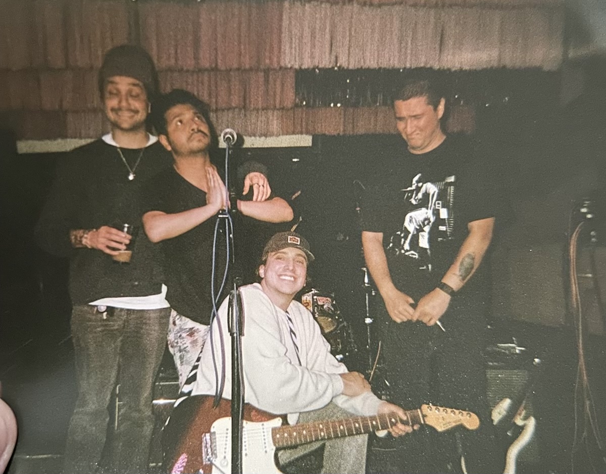 Four band members around their instruments in a faded photograph