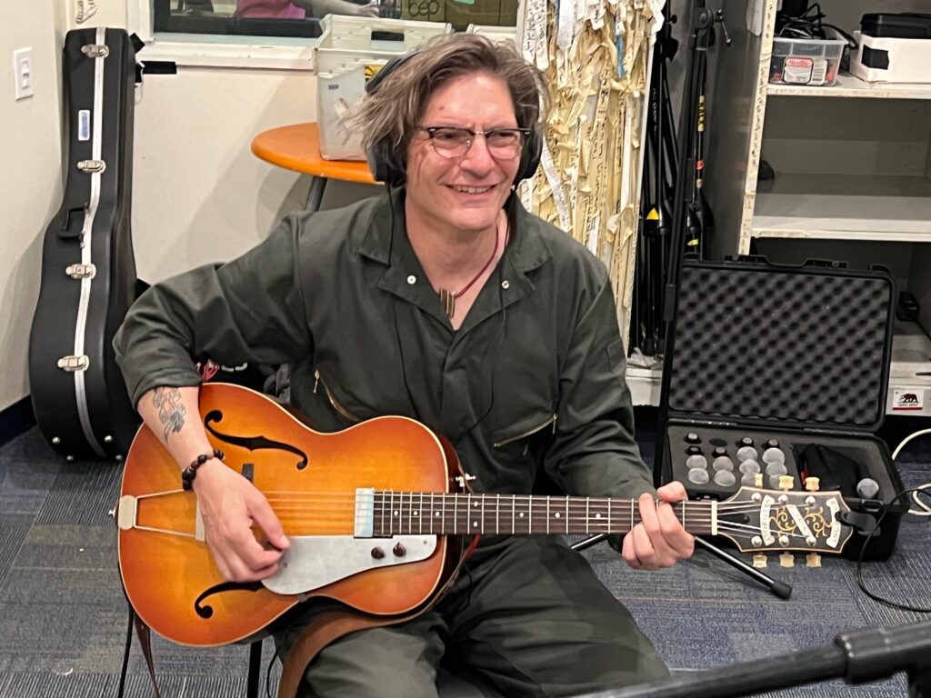 A man sitting with an electric guitar in the radio studio recording