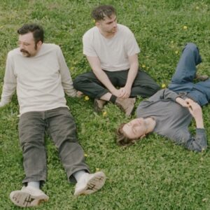 Three members of band sitting on grass outside.