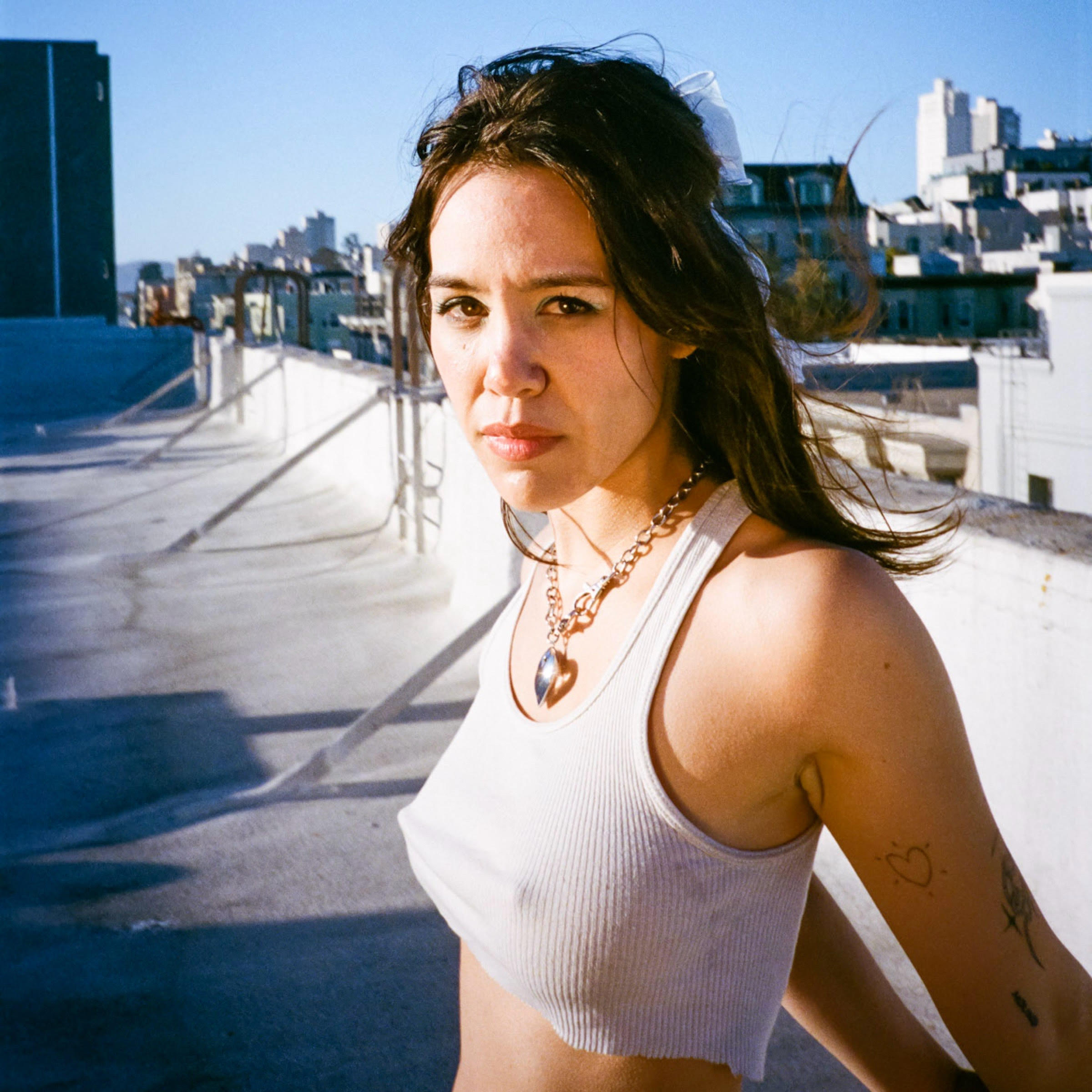 Woman wearing a necklace and white tank top standing on the roof of a city building