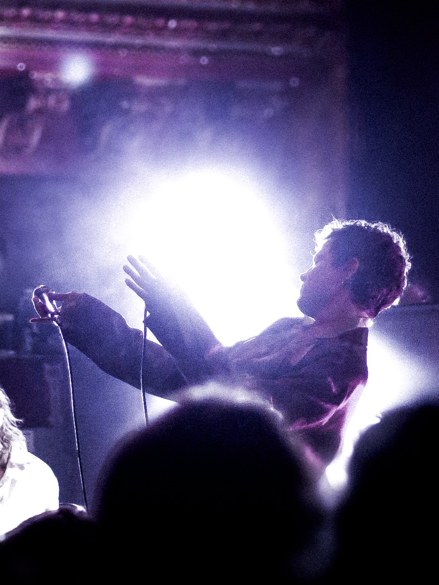 Musician swaying holding a microphone under a spotlight in a theater