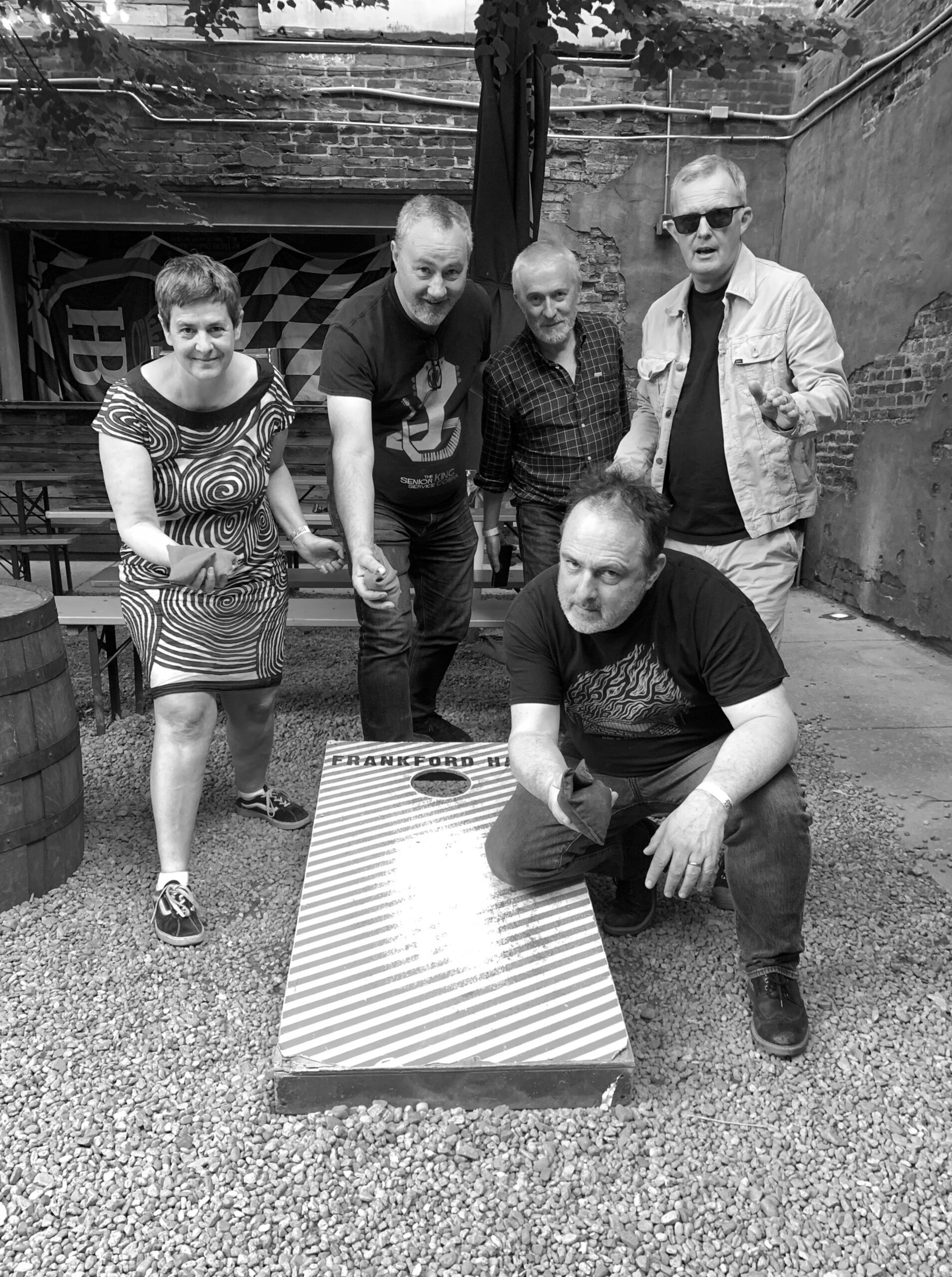 Black and white image of 5 people standing around a cornhole set, posing.