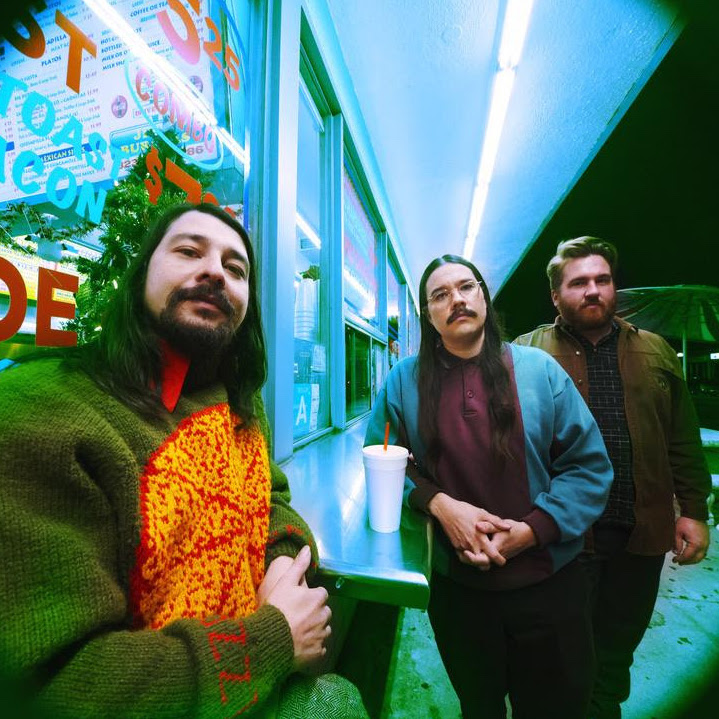 Three members of band outside a mini mart.