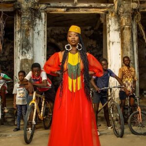 Dobet Gnahoré standing outside in front of children on bikes.