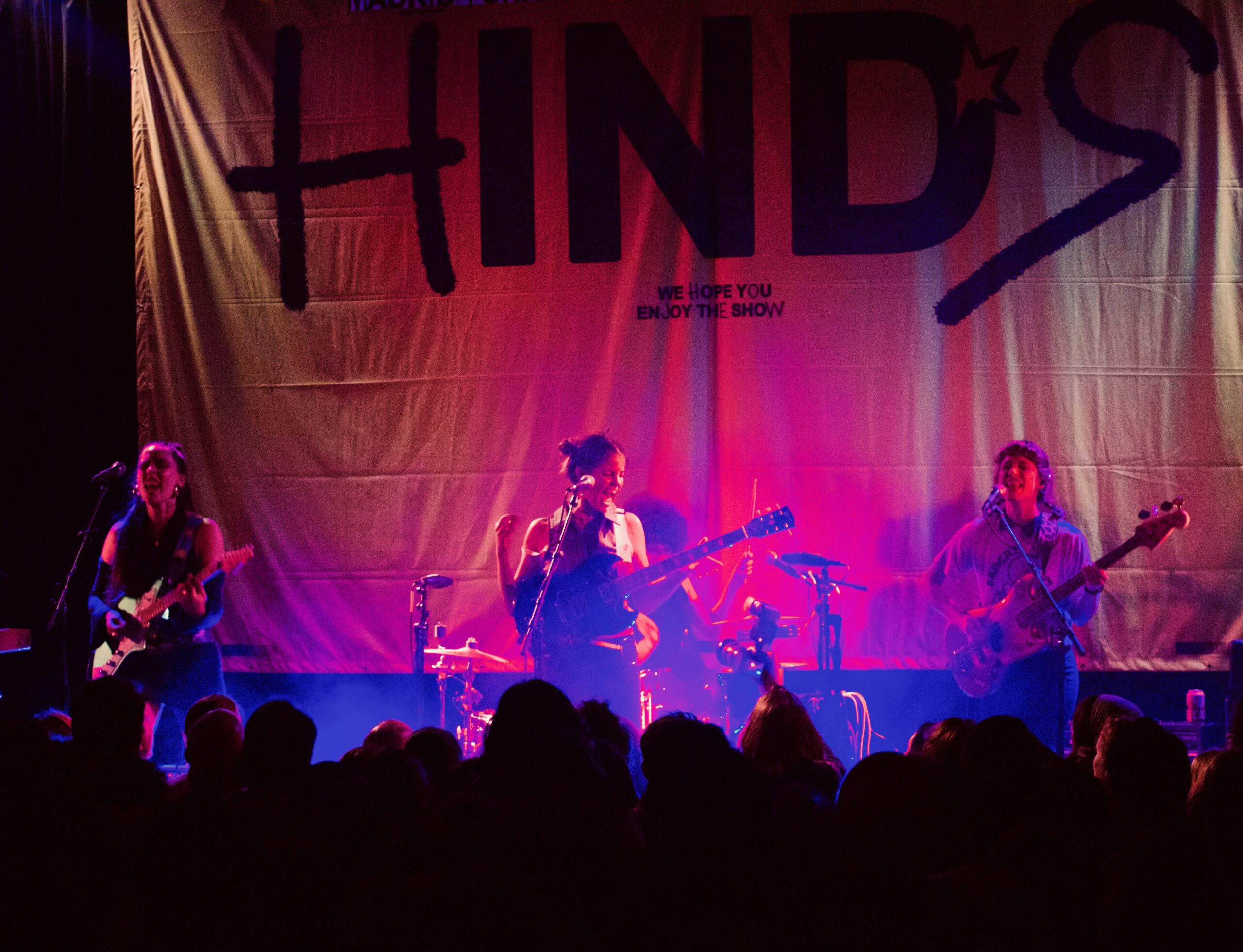 Four member rock band Hinds on stage in front of a large banner of their name