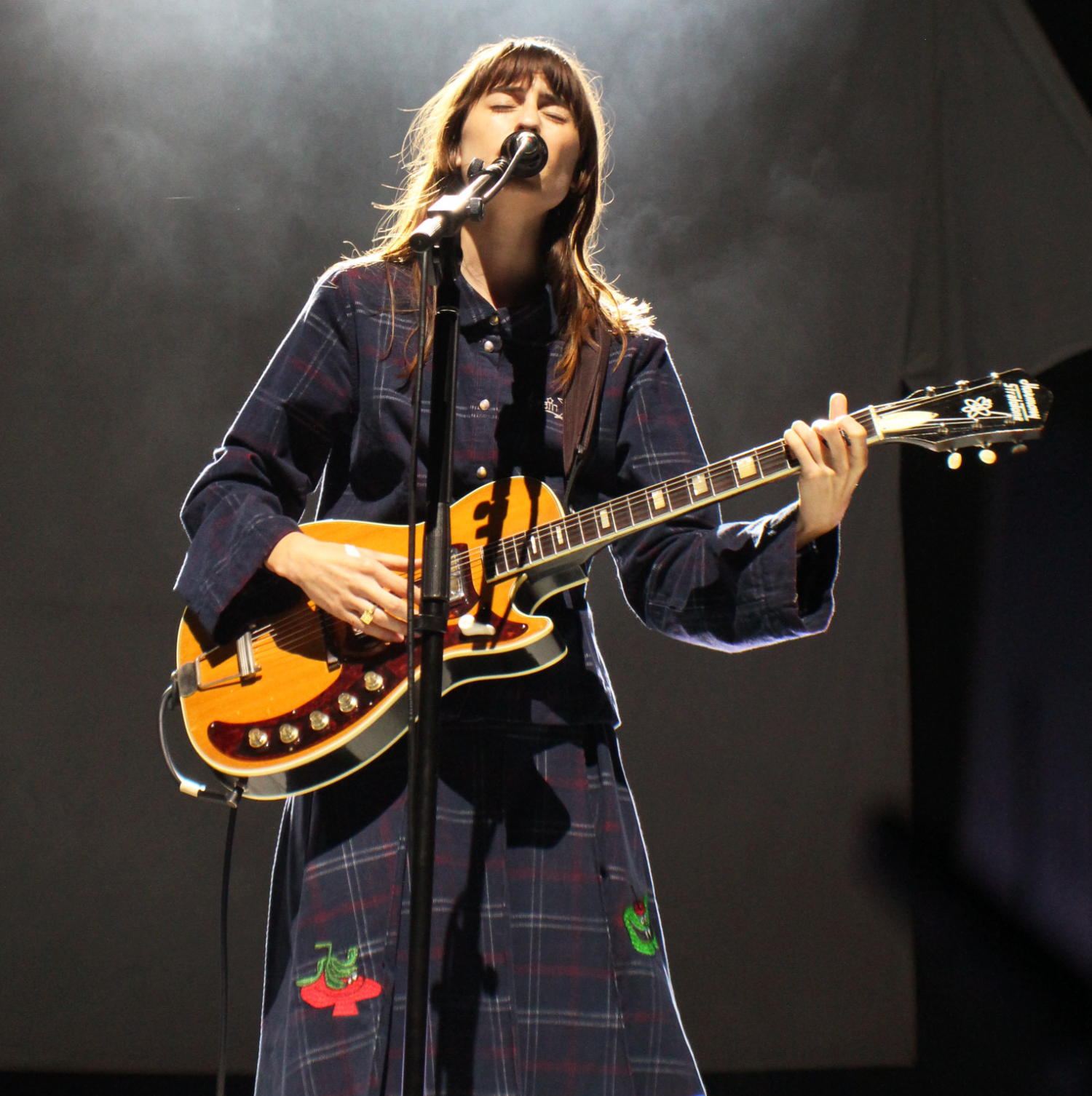 Woman performing on stage, playing electric guitar and singing into a microphone