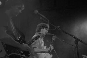 Black and white photo featuring two guitarists singing in front of microphones on stage