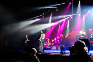 Four member rock band performing on stage under lights