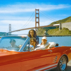 Band in a red mustang on the road.