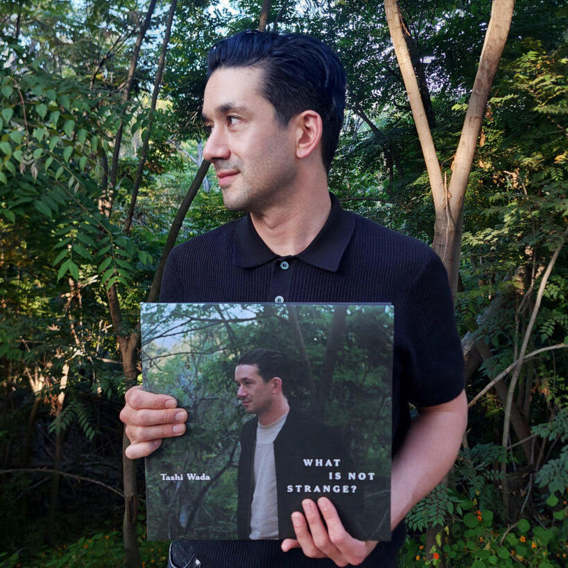 Tashi Wada standing in nature with album in hand.