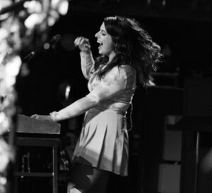 Member of rock band La Luz playing the keyboard and singing on stage set to black and white