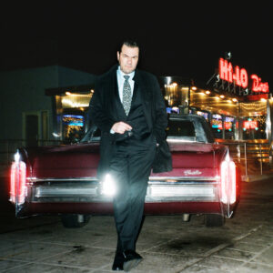 Ant standing outside in front of vintage Cadillac.