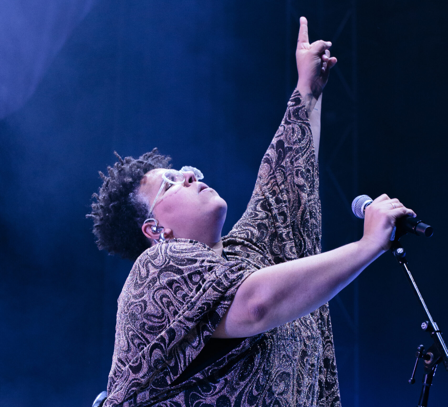 Musician Brittany Howard looking up and pointing straight into the air while on stage and holding a microphone in the other hand