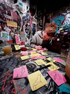 A man sketching on post-its at a table in a bar covered in graffiti