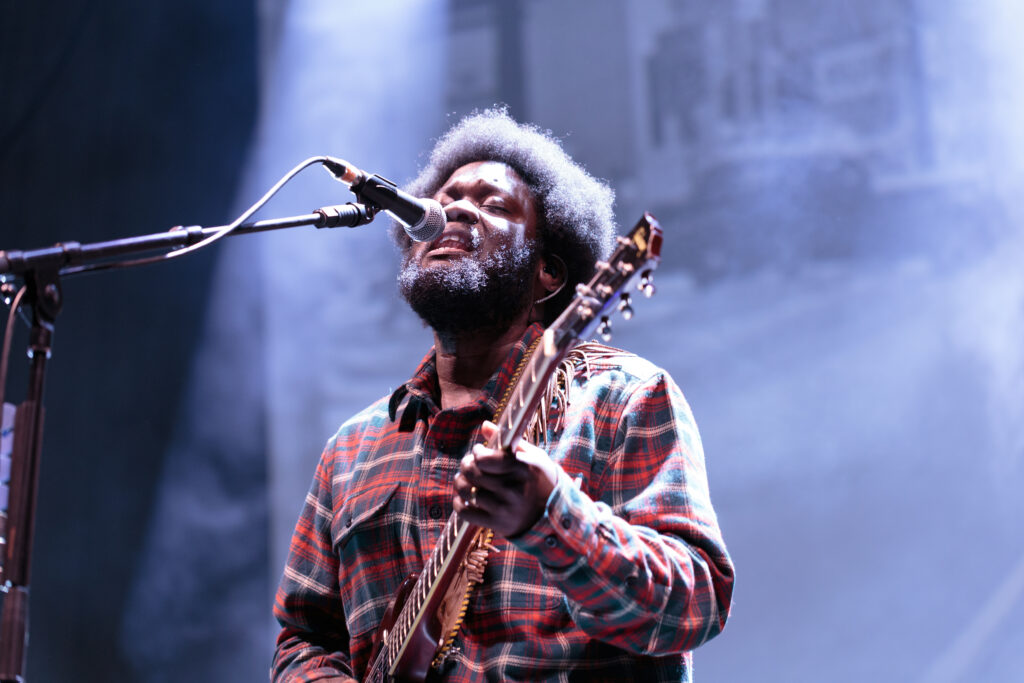 Musician Michael Kiwanuka, wearing a red flannel shirt, plays guitar and sings on stage at The Greek Theater in Berkeley CA