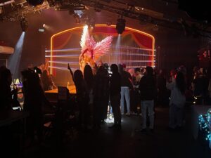 A performing in a large wings on a cat walk surrounded by a crowd