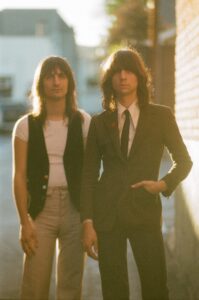 Both members of The Lemon Twigs standing side by side outside a house