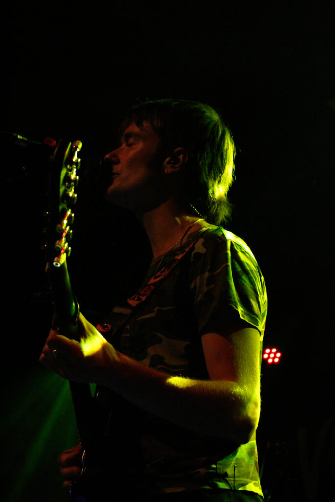 Brandon Hagen of Vundabar singing and playing guitar in stage in green light