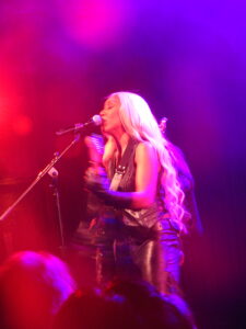 Blurred photos with red lights surrounding musician Fousheé singing and playing guitar