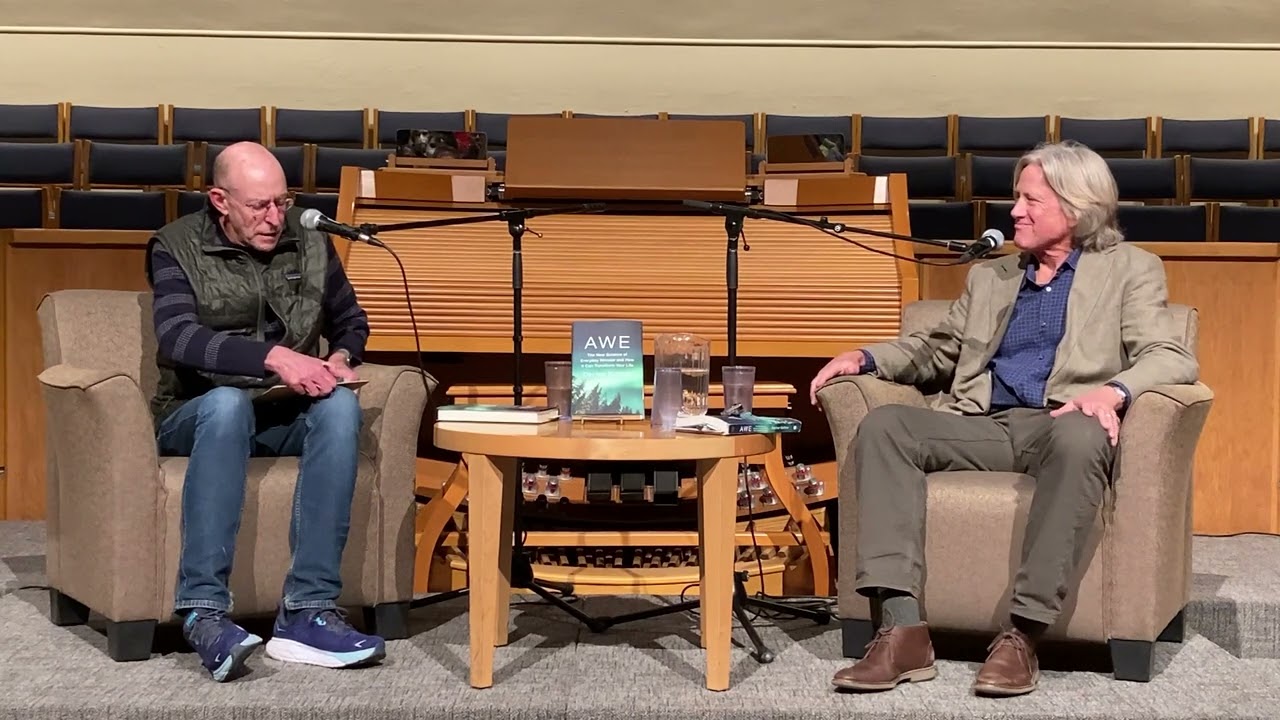 Two men sitting in chairs opposite eachother on stage