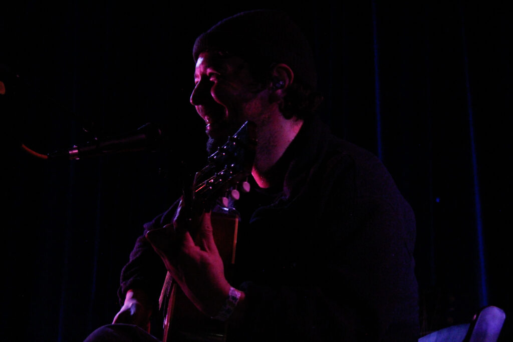 Robin Pecknold smiling while playing guitar on stage