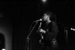 black and white photo of a female musician singing while plating guitar on stage