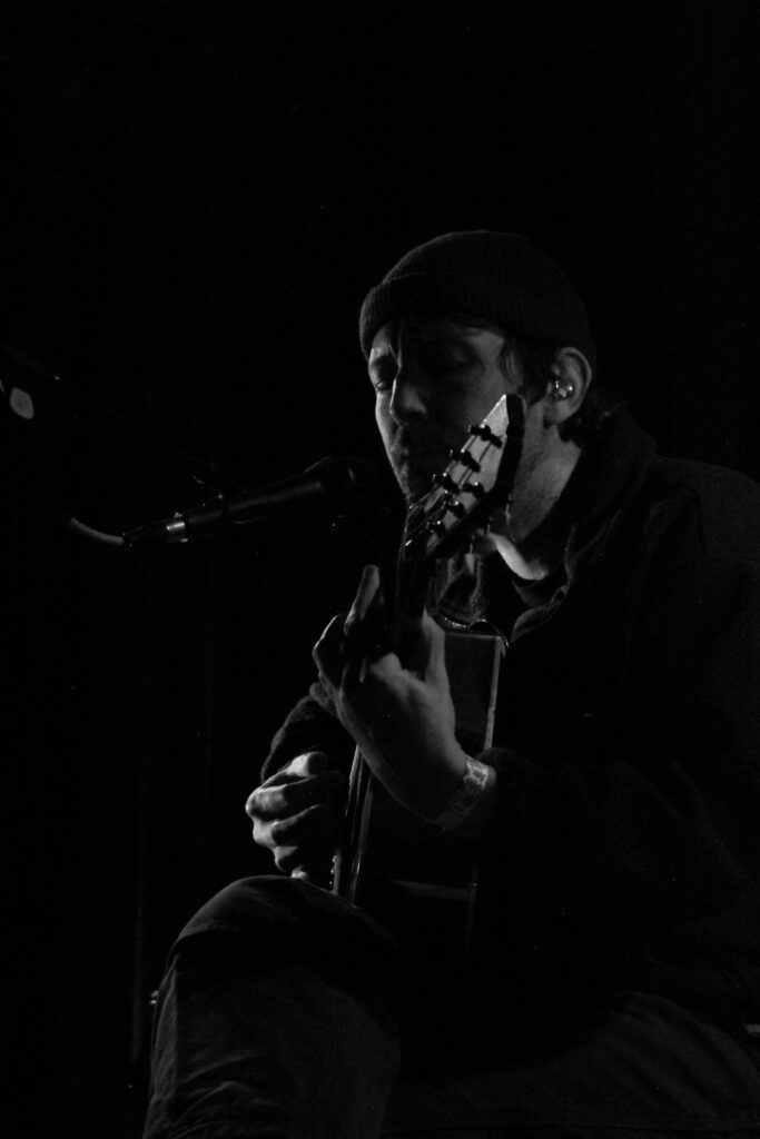 Robin Pecknold, seated, singing while playing guitar on stage