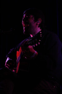 Robin Pecknold, seated, singing while playing guitar on stage