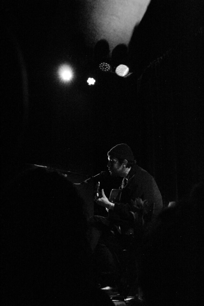 Robin Pecknold, seated, singing while playing guitar on stage